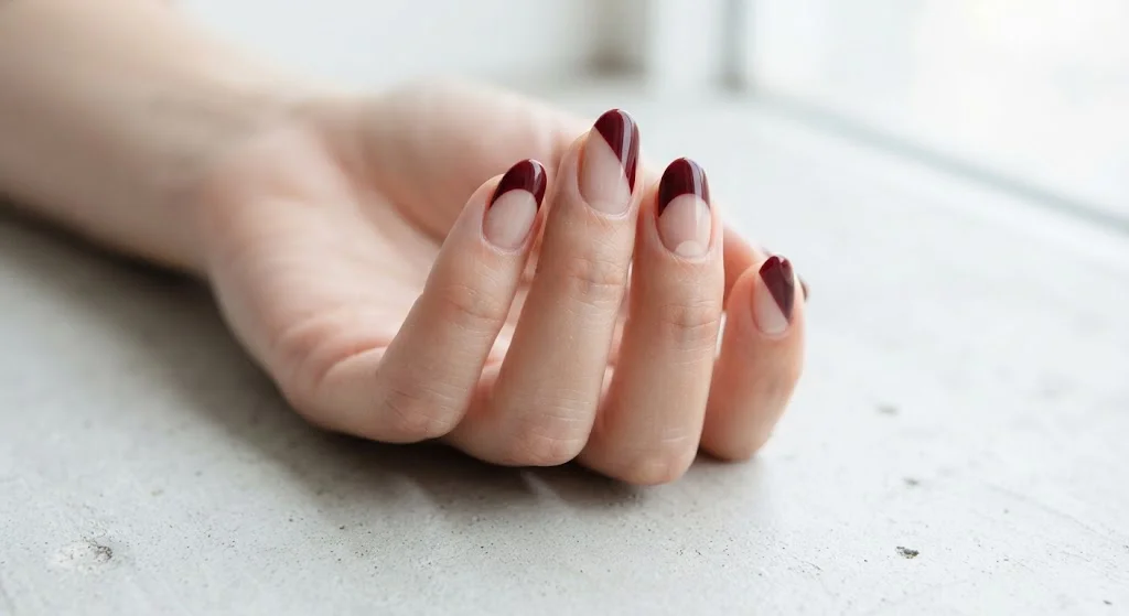 Modern maroon negative-space nail design with curved neutral sections.